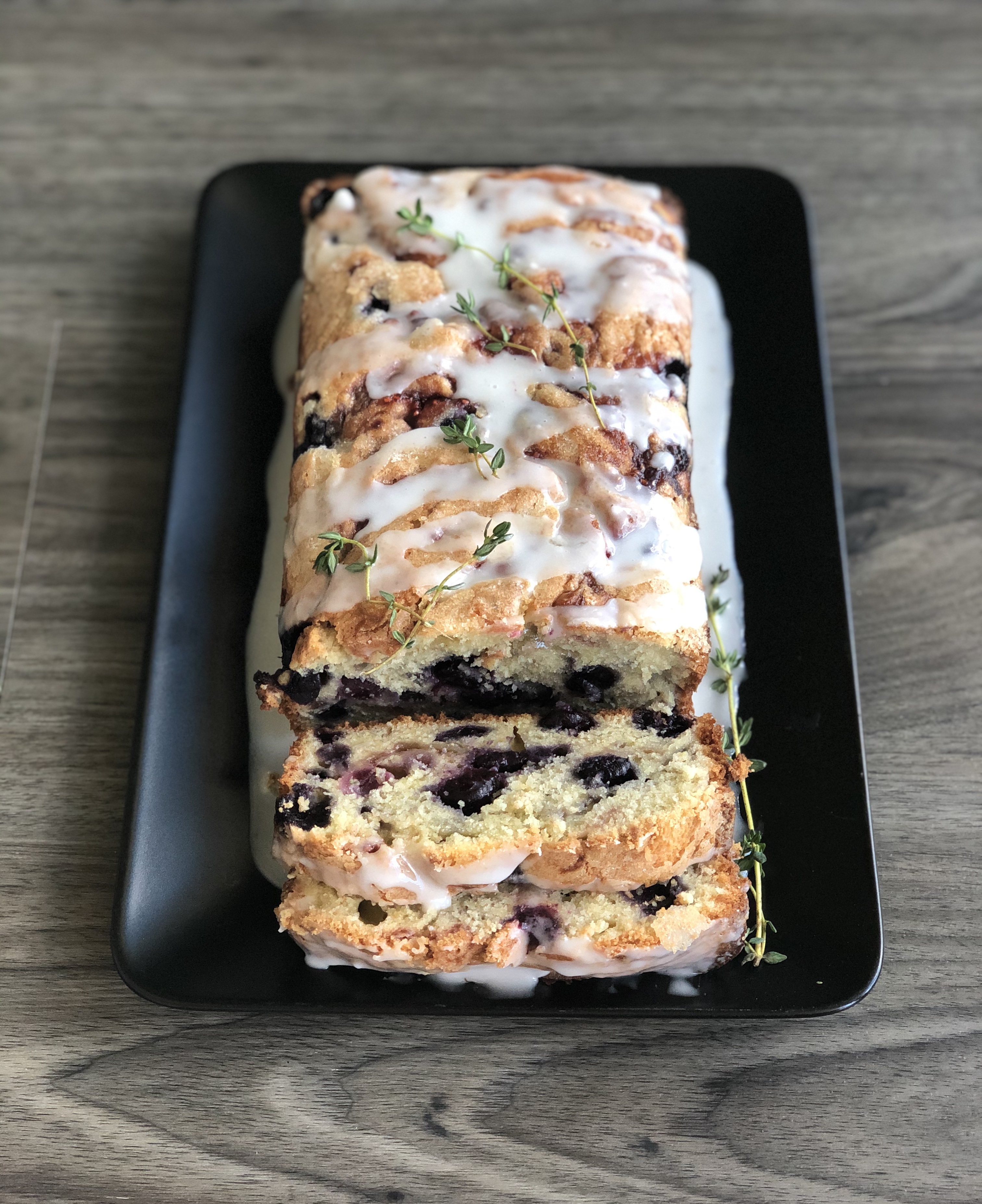 Blueberry Loaf cake sliced and drizzled with lemon glaze and fresh thyme leaves.
